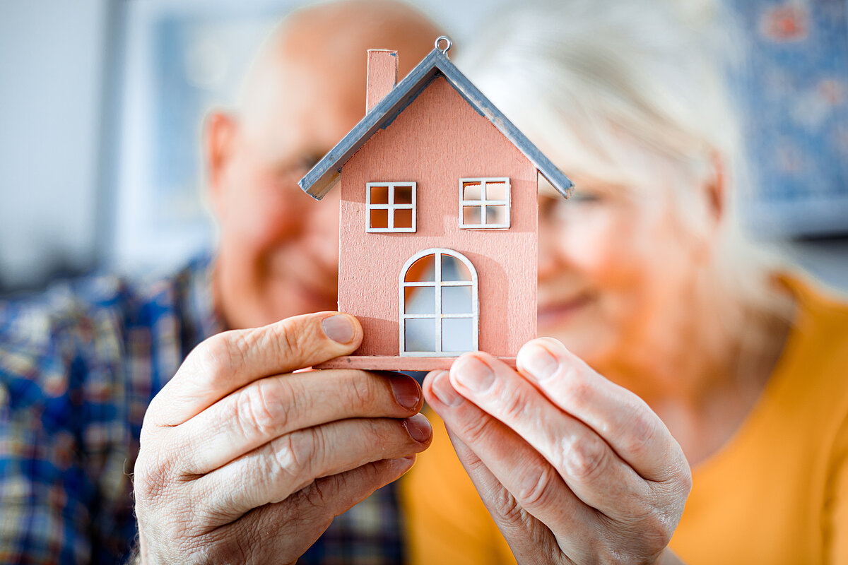 Seniorenpaar hält Modell eines Hauses in die Kamera