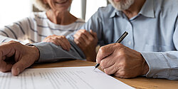 Nahaufnahme eines Seniorenpaares, das an einem Tisch sitzt und einen Vertrag unterschreibt
